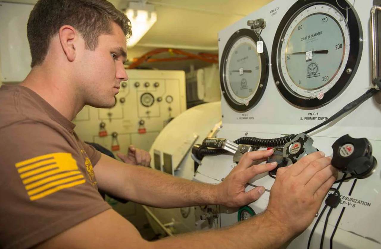 An operator adjusts valves on a chamber control panel beneath two large gauges.