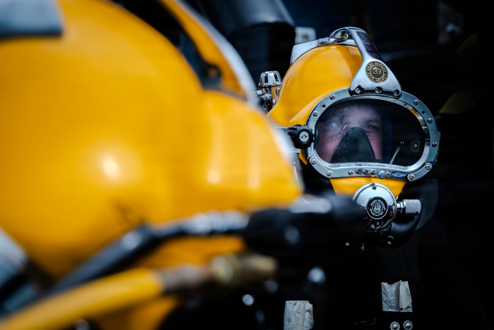 A commercial diver wearing a yellow helmet, with another diver in the foreground.