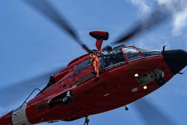 A rescue helicopter overhead, with a crew member at the open side door.